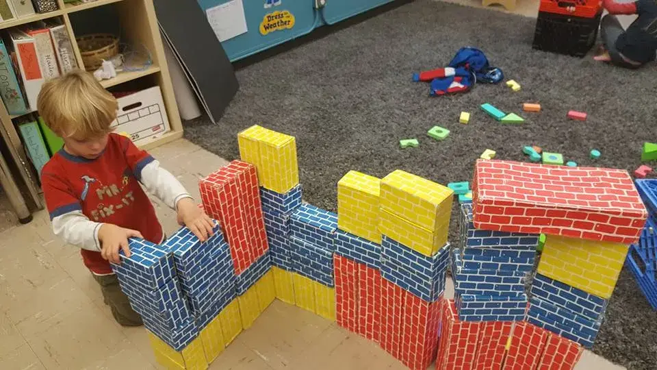 Children building a large structure with colorful patterned blocks.