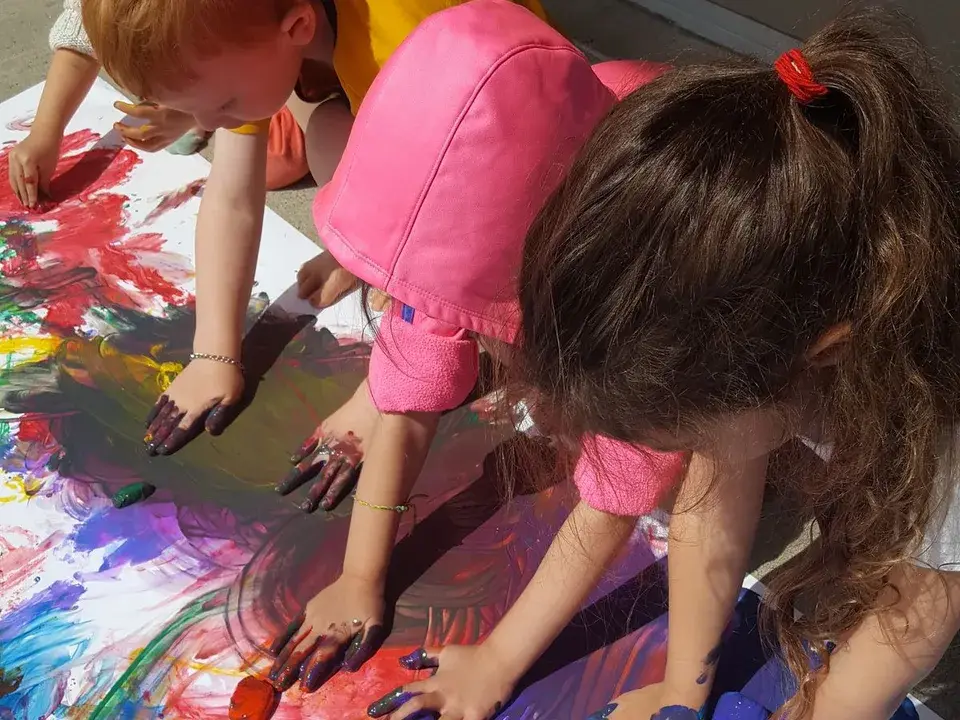 Children adding colorful paint to a large shared artwork.