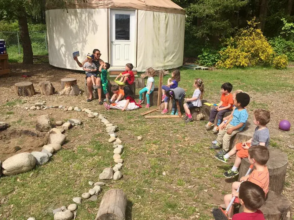 Children sitting in a circle with an adult in an outdoor learning space.