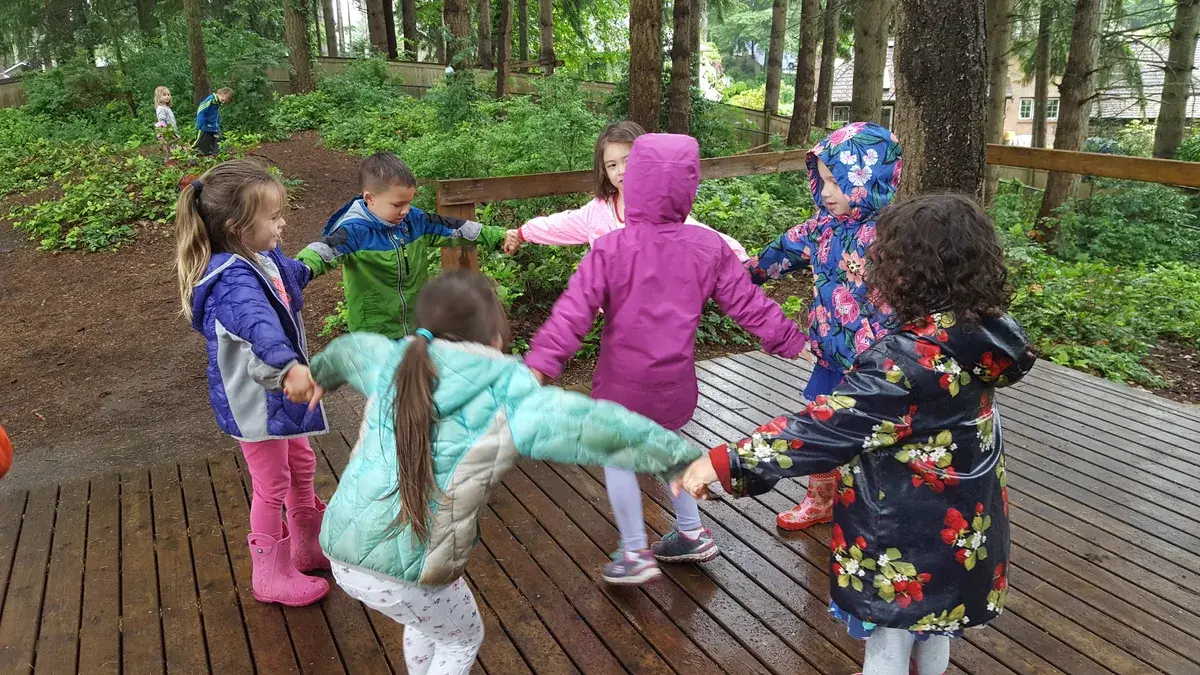 Children and adults moving together on a deck surrounded by trees.