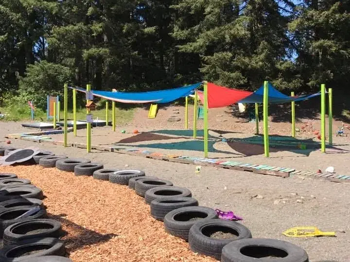 A school outdoor play area with a tire-lined path and tall trees.