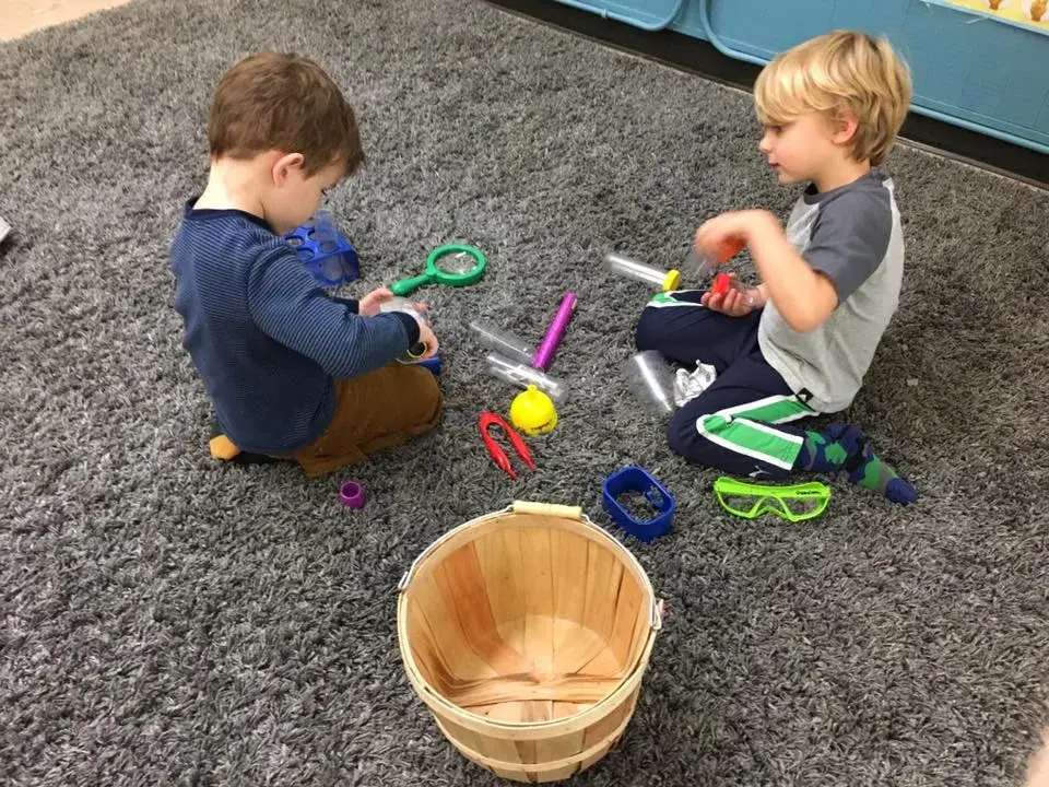 Two children using bowls and small tools together during outdoor play.