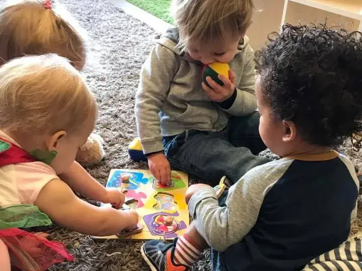 Young children playing together with colorful toys on a classroom rug.