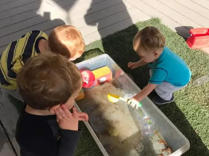 Children exploring water together at an outdoor activity table.